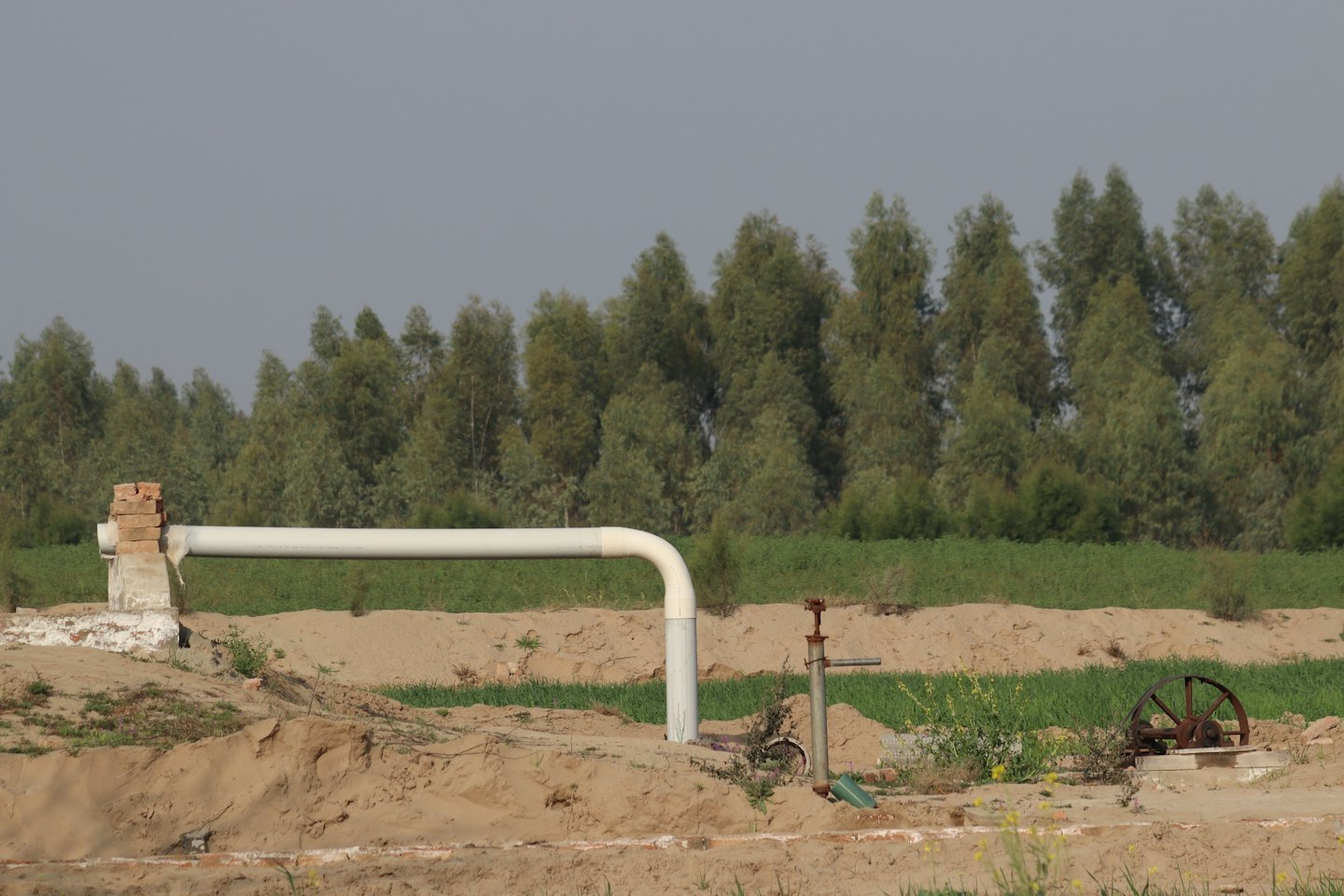Una tubatura industriale bianca attraversa un fosso di terra aperto.